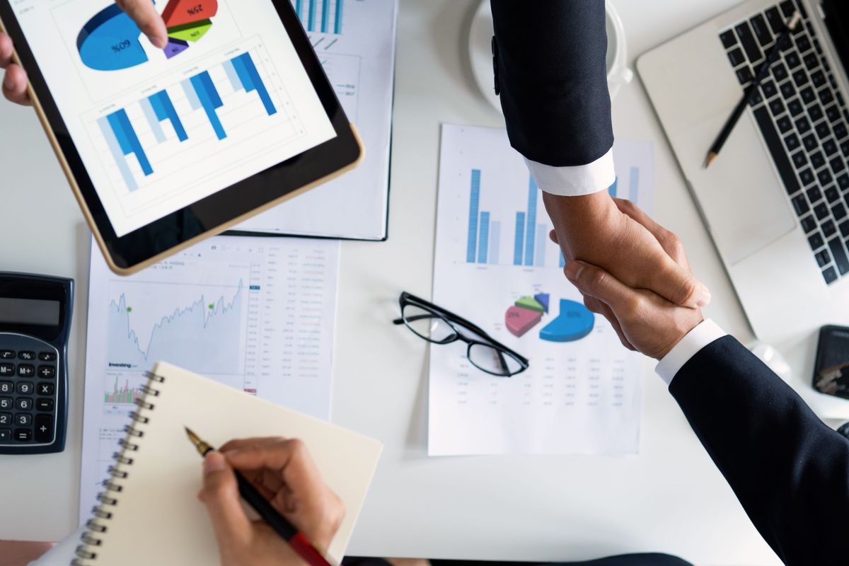 Business handshake over reports and charts, representing B2B account management, client retention and data-driven operations