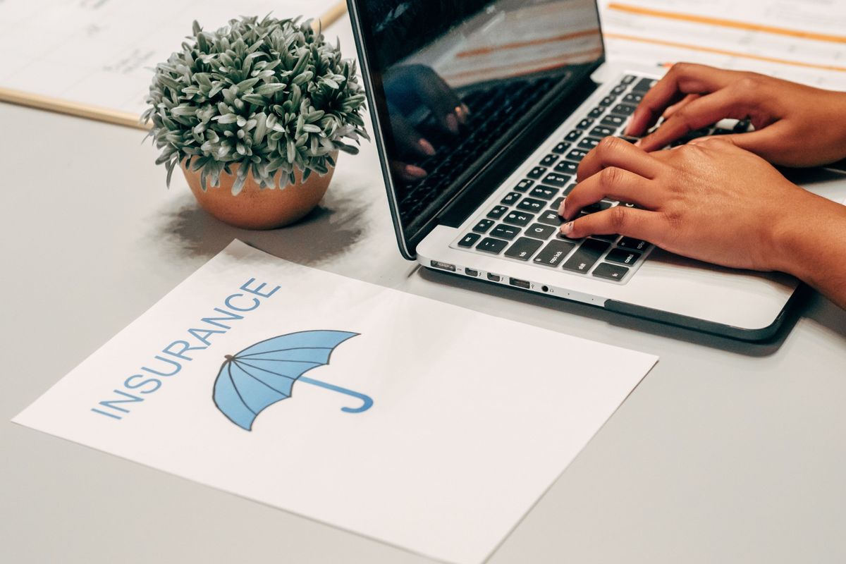 Laptop beside a commercial insurance policy document with an umbrella icon, representing Property & Casualty insurance, policy administration and risk analysis